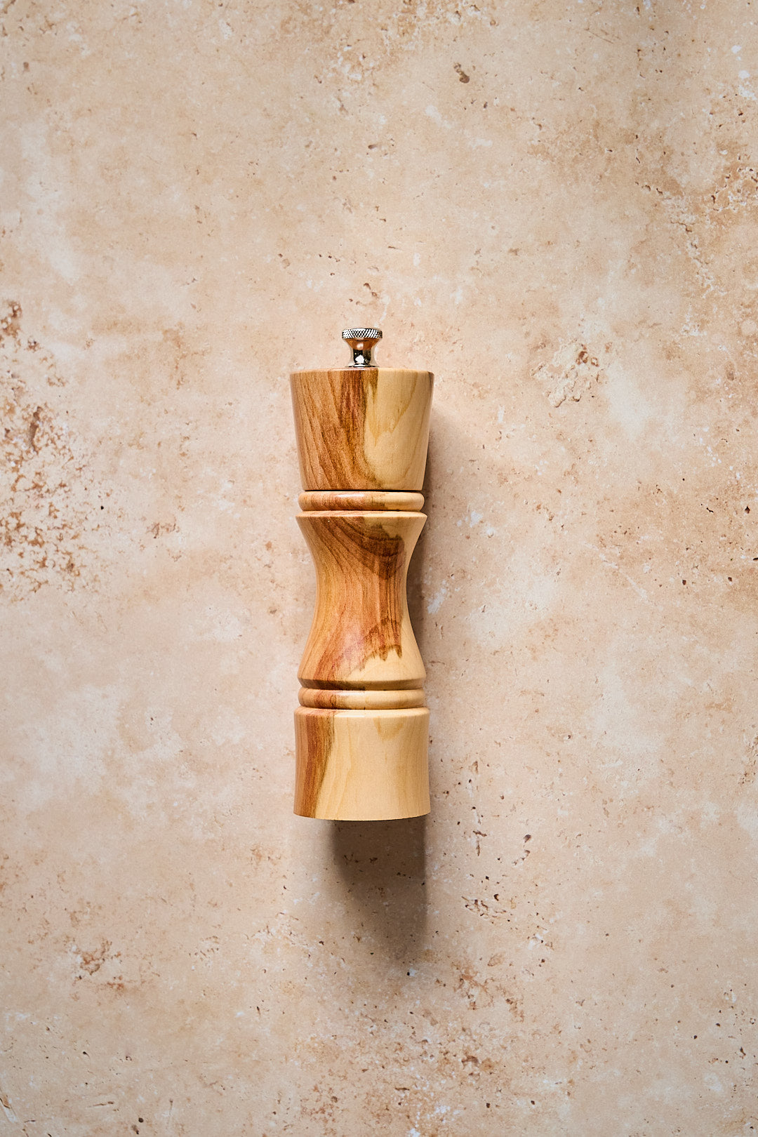 The small handmade pepper mill on a warm stone background