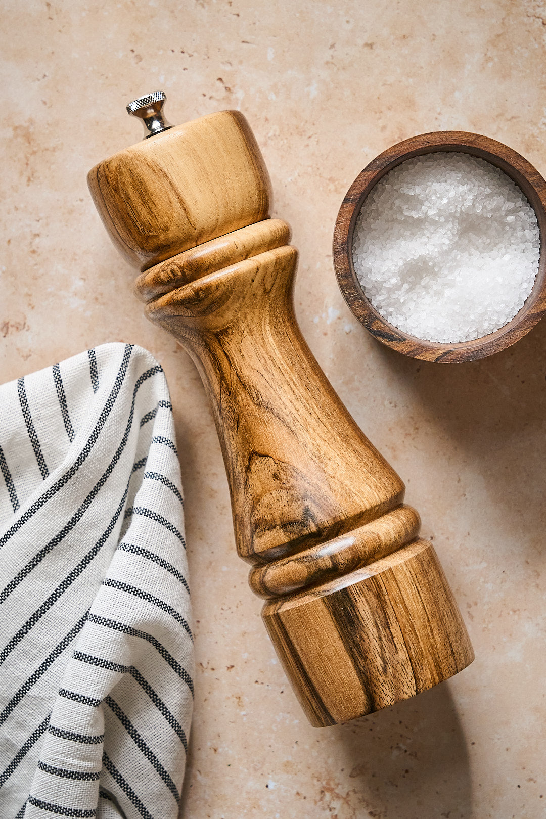 Milan big pepper grinder made from American walnut beside a bowl of salt on a countertop with a striped towel.