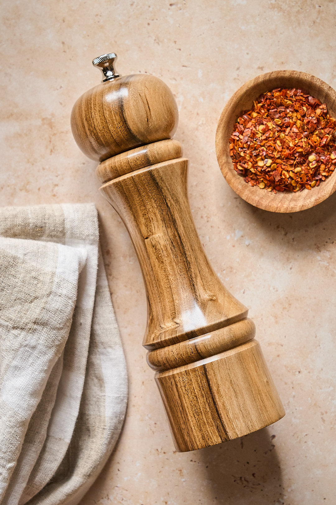 Handmade walnut pepper mill on a counter with a bowl of spices.