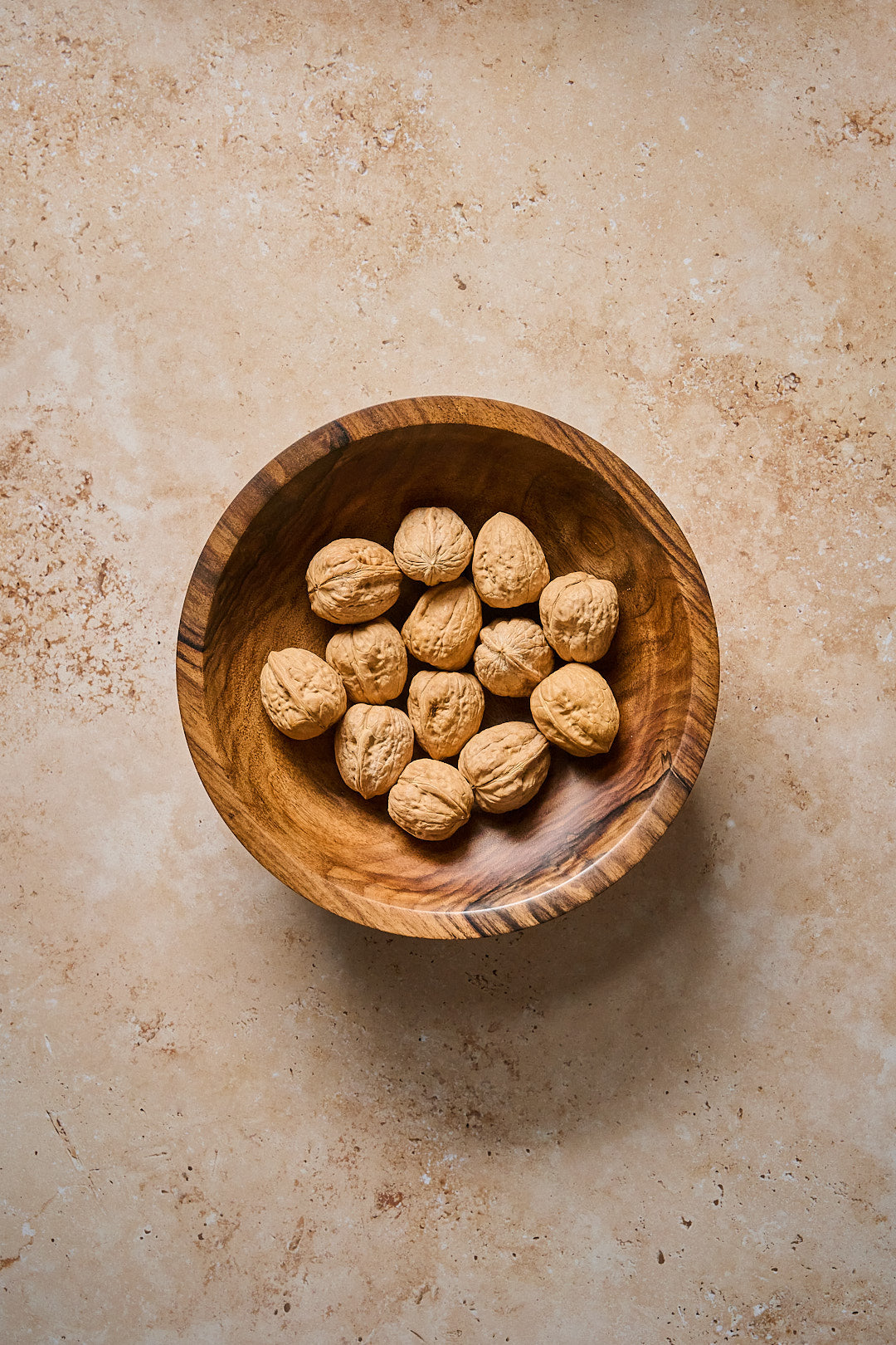 Helsinki Handmade Walnut Bowl filled with walnuts on a textured surface.