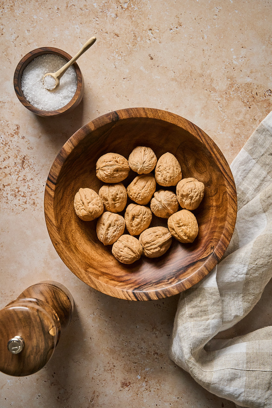 The handmade walnut bowl full of walnuts next to earth toned linens, salt, and pepper