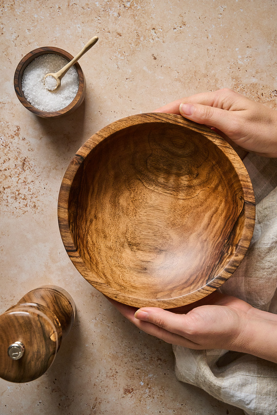 Hands holding the handmade walnut bowl over a stone surface in a kitchen