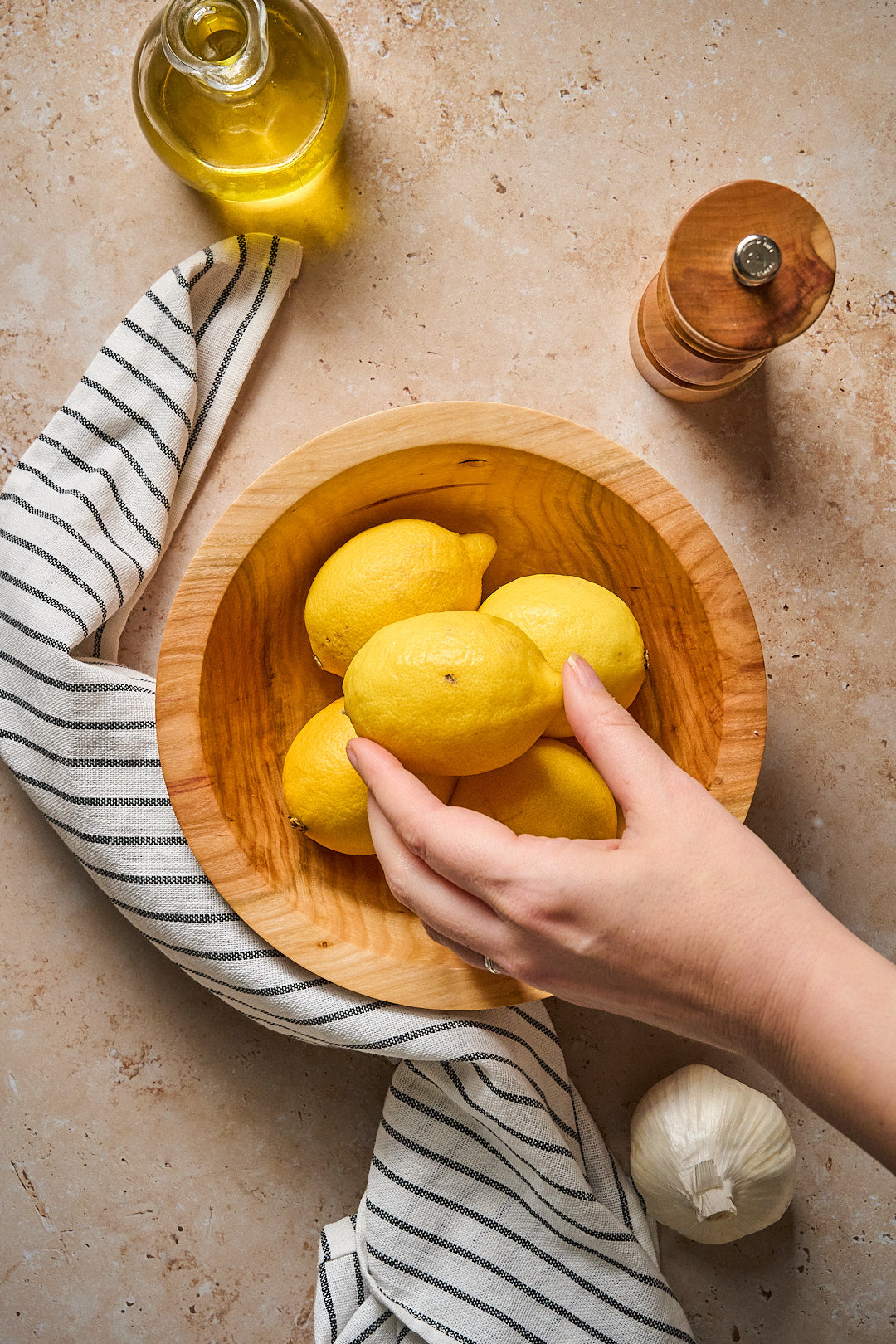 A hand reaching into the handmade wooden bowl to pick up a lemon.