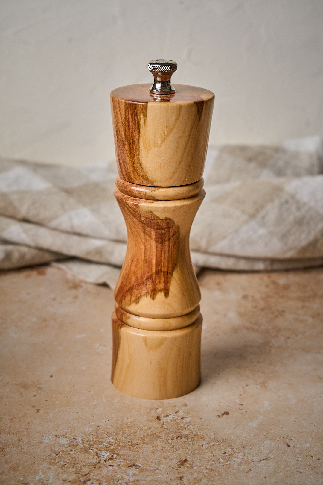 Side view of small handmade pepper mill, showing natural variations in plum wood
