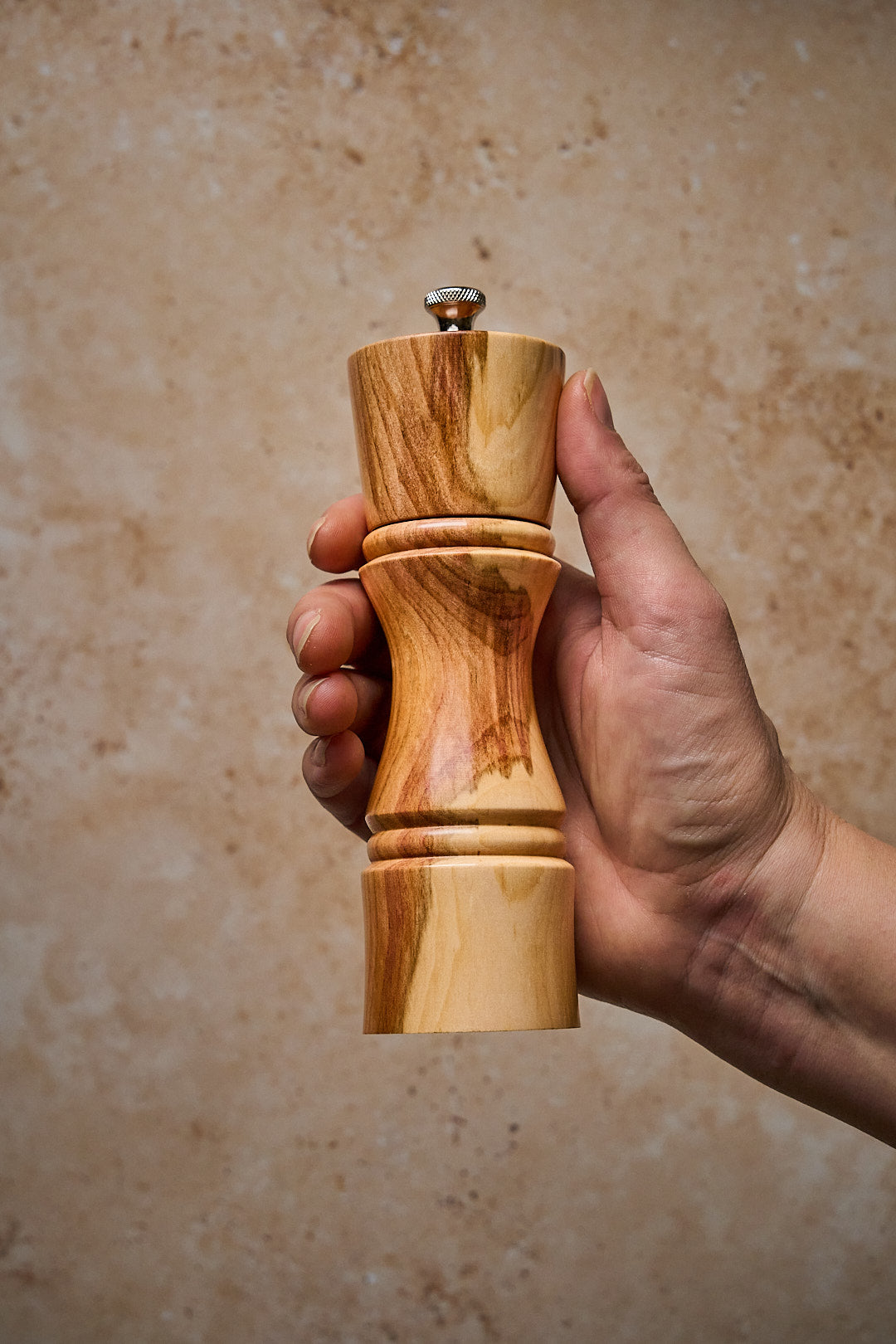 A hand holding the small handmade pepper mill to show scale