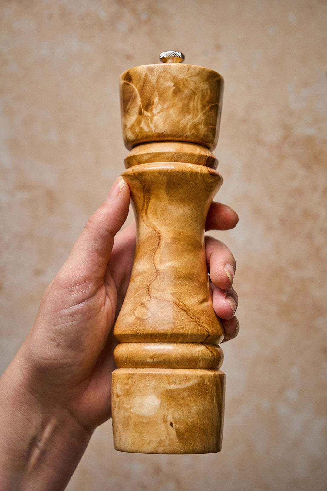 A hand holding a light birch handmade pepper grinder