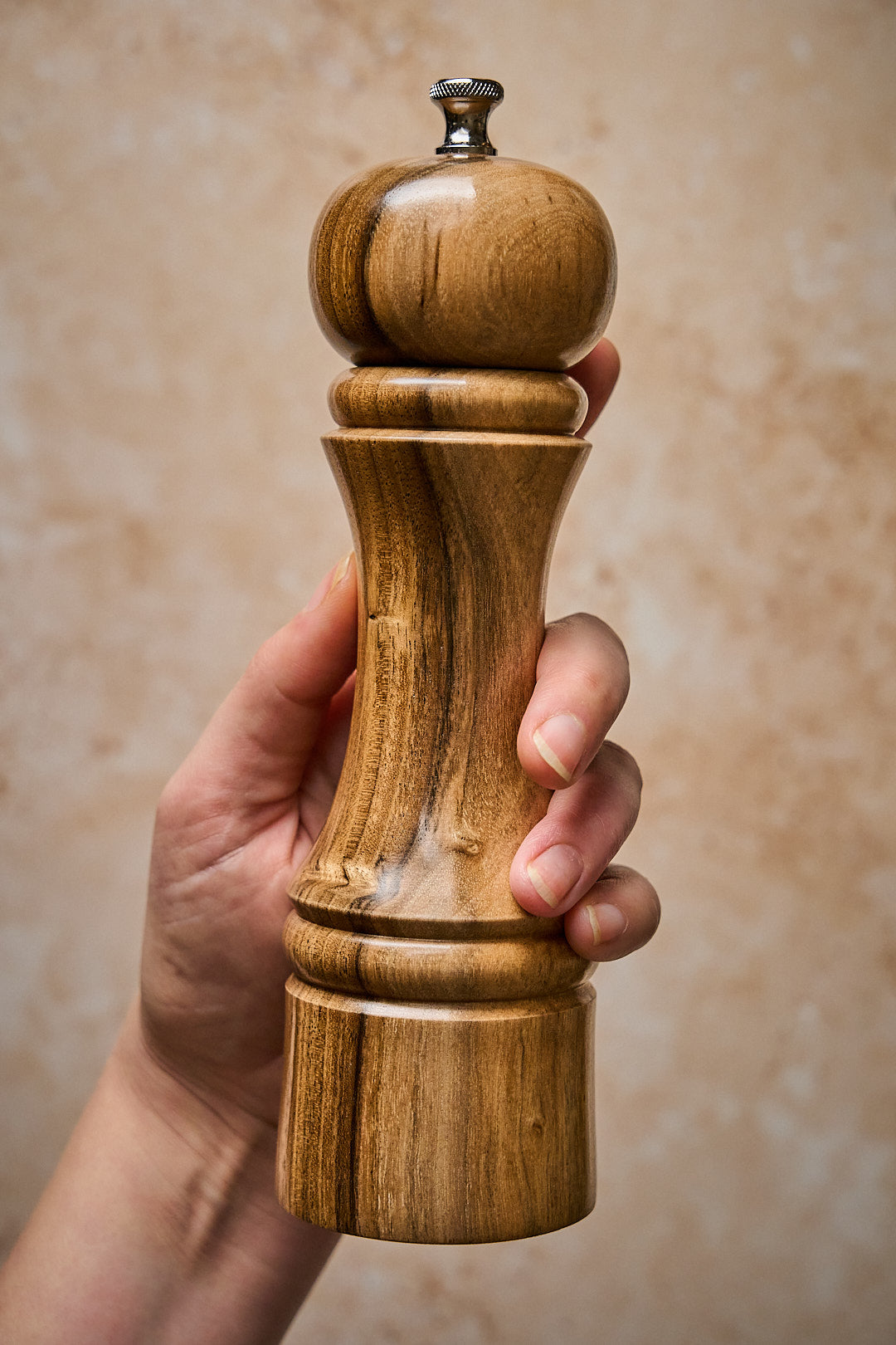 Handmade walnut pepper mill held in hand, showcasing its elegant design and smooth finish.