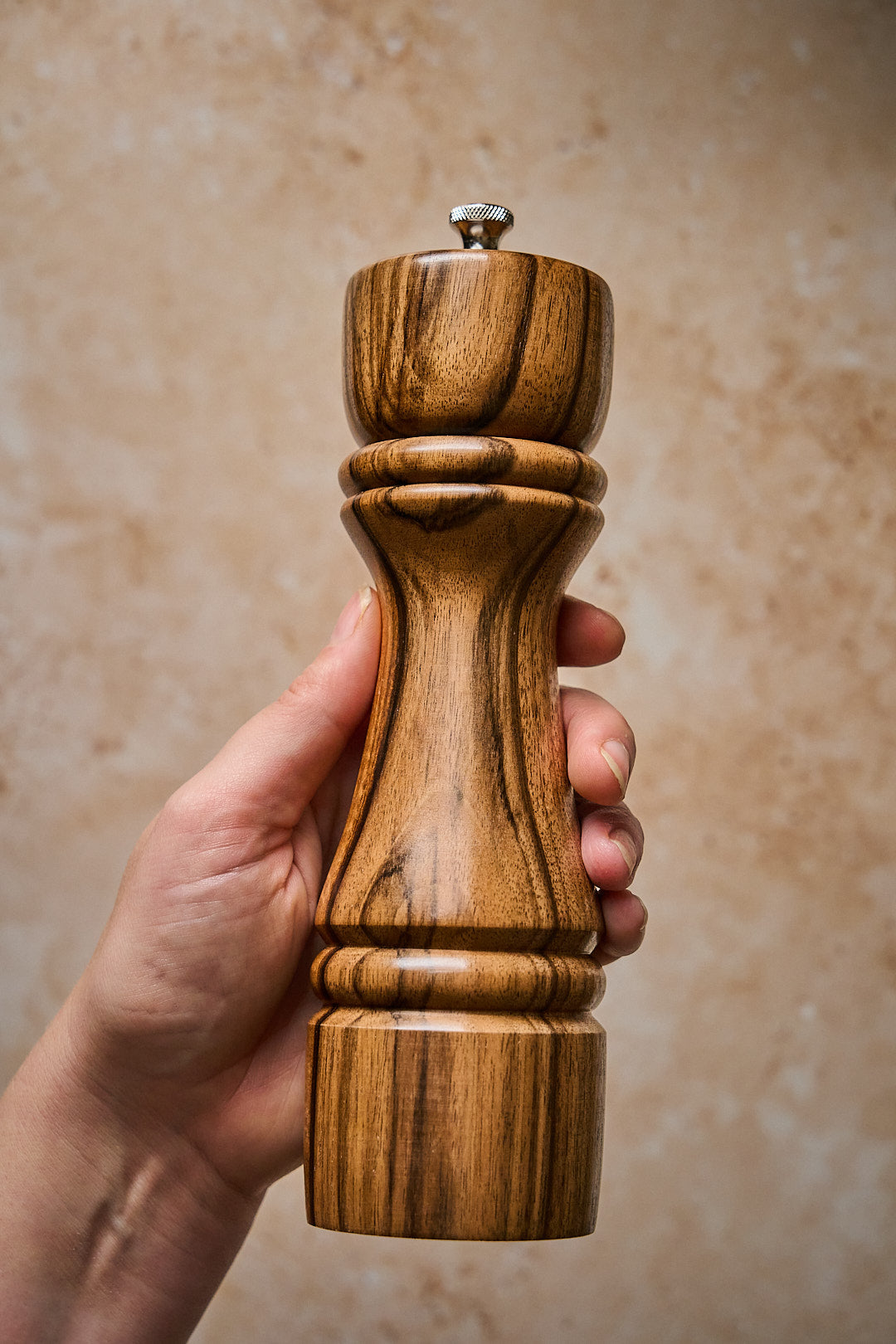 A hand holding a handmade walnut pepper grinder