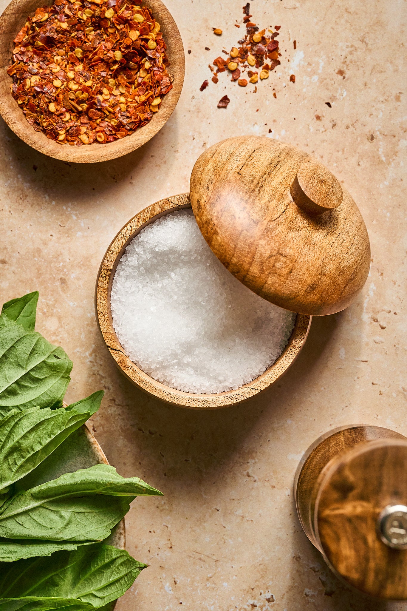 The wood salt cellar opened and filled with salt next to herbs and spices