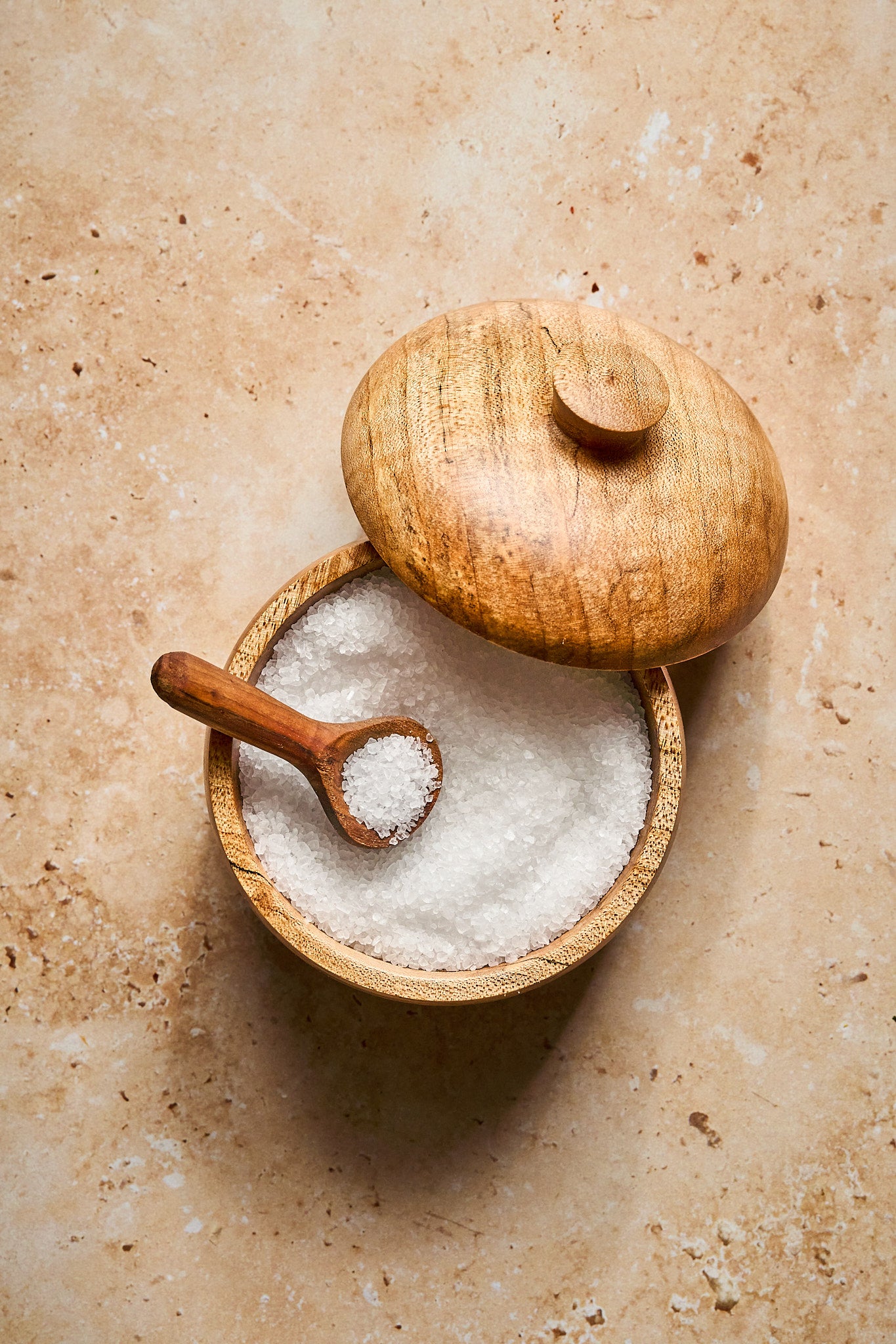 A tiny spoon scoops coarse salt from the wood salt cellar