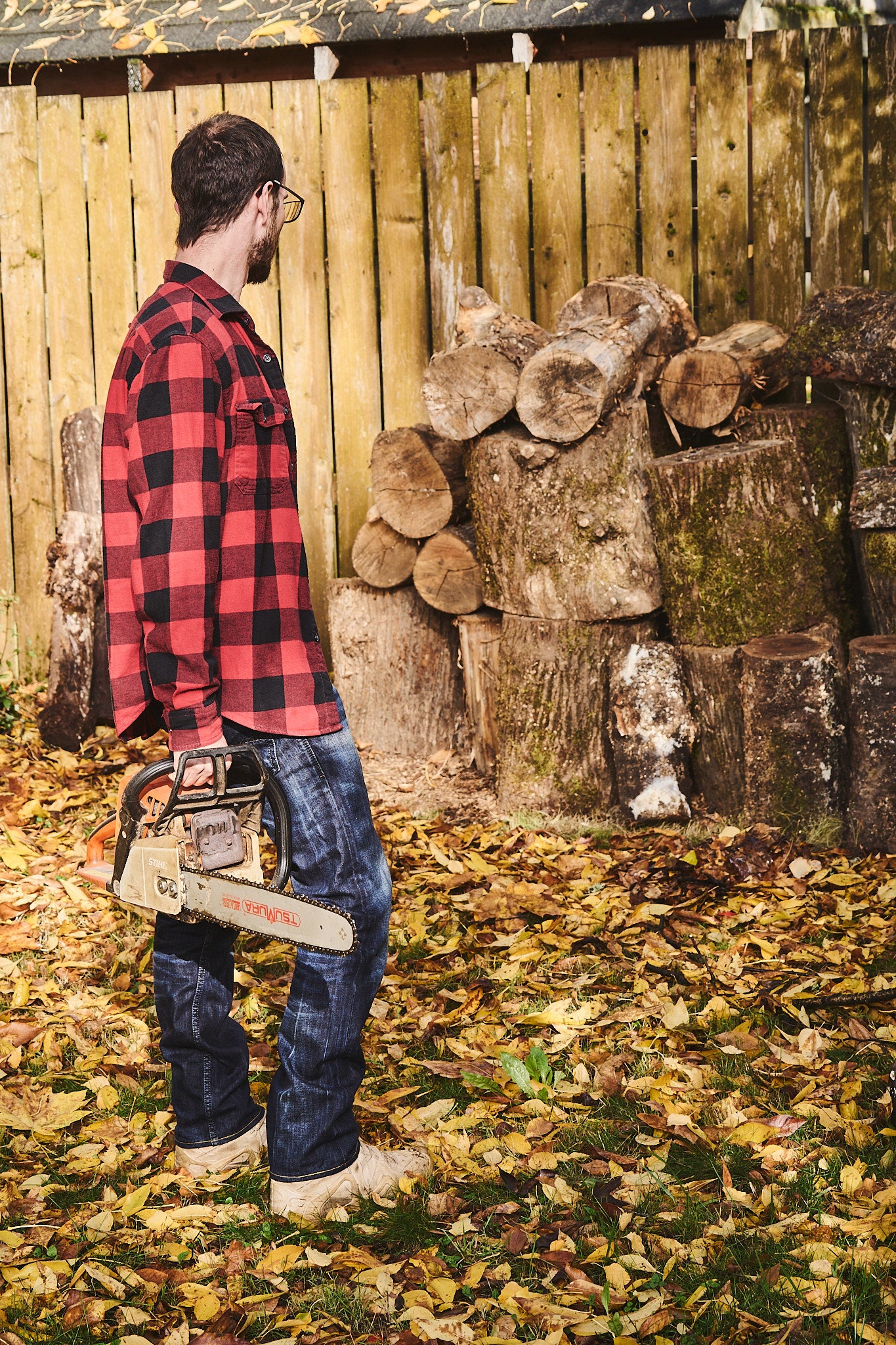 The artist holds a chainsaw while selecting a piece of wood to work with