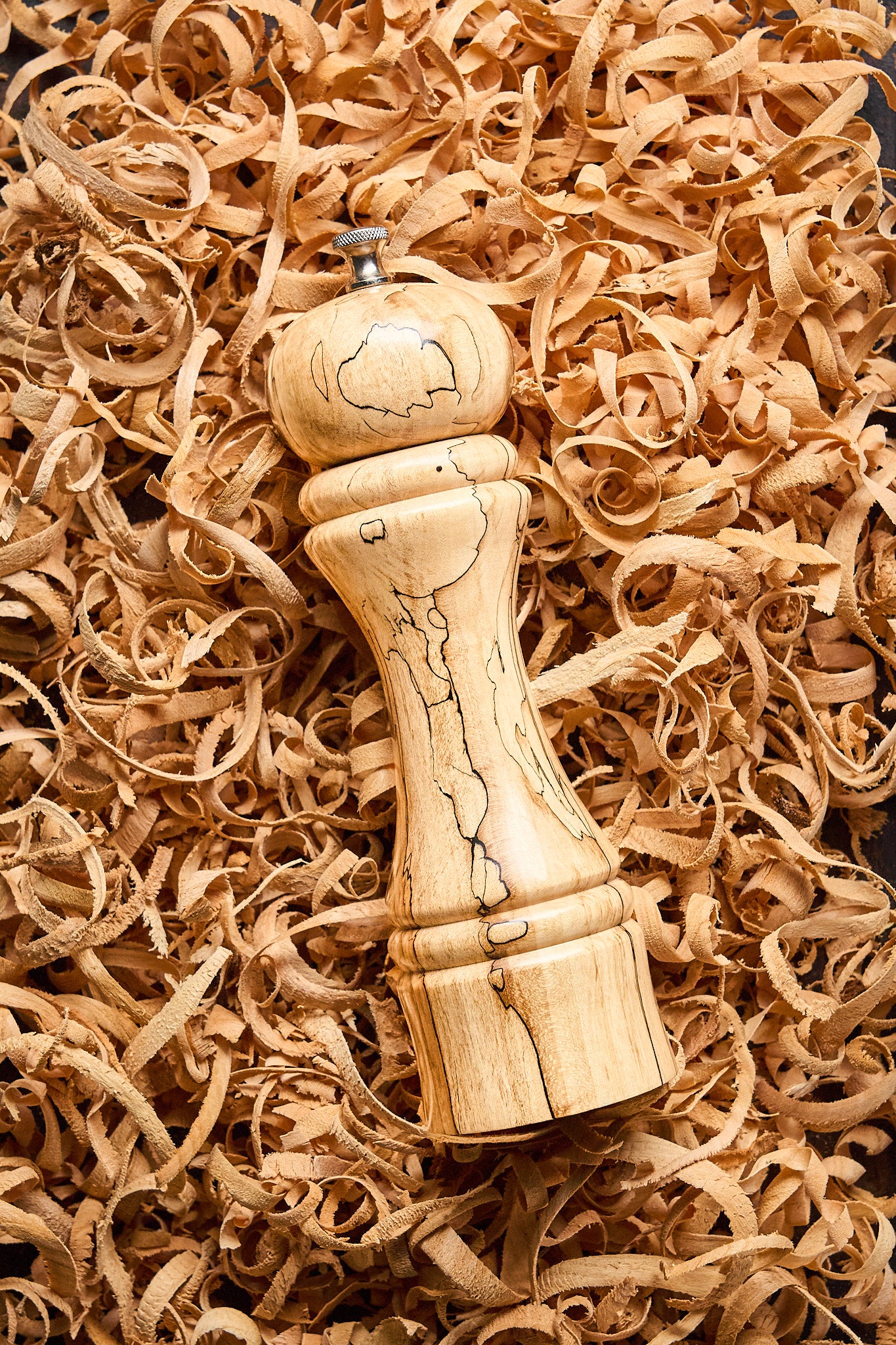 Overhead shot of the tall pepper mill resting in wood shavings left behind by the artisan