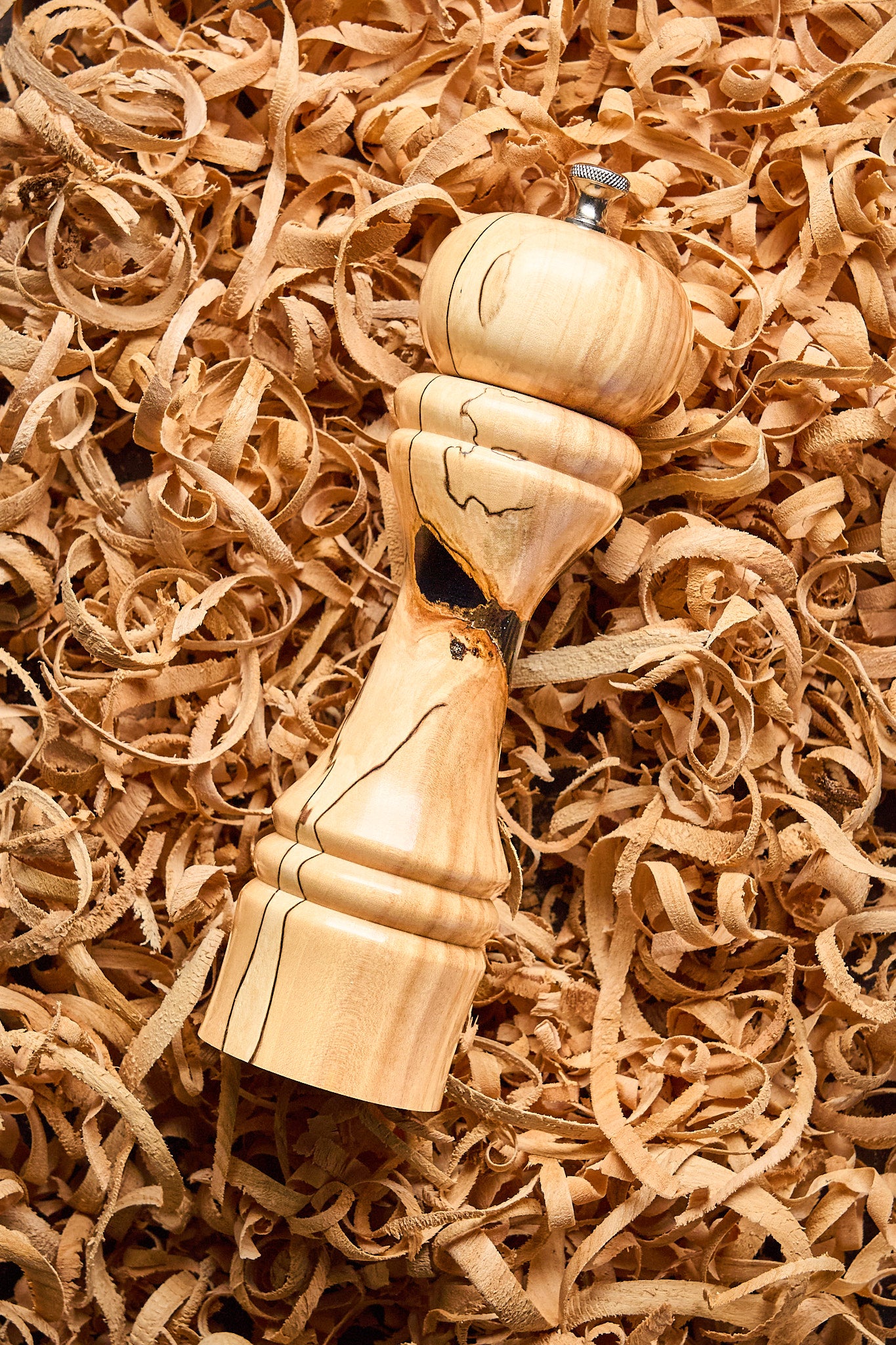 The unique pepper grinder rests in a bed of wood shavings, showing the work that went into making it by hand