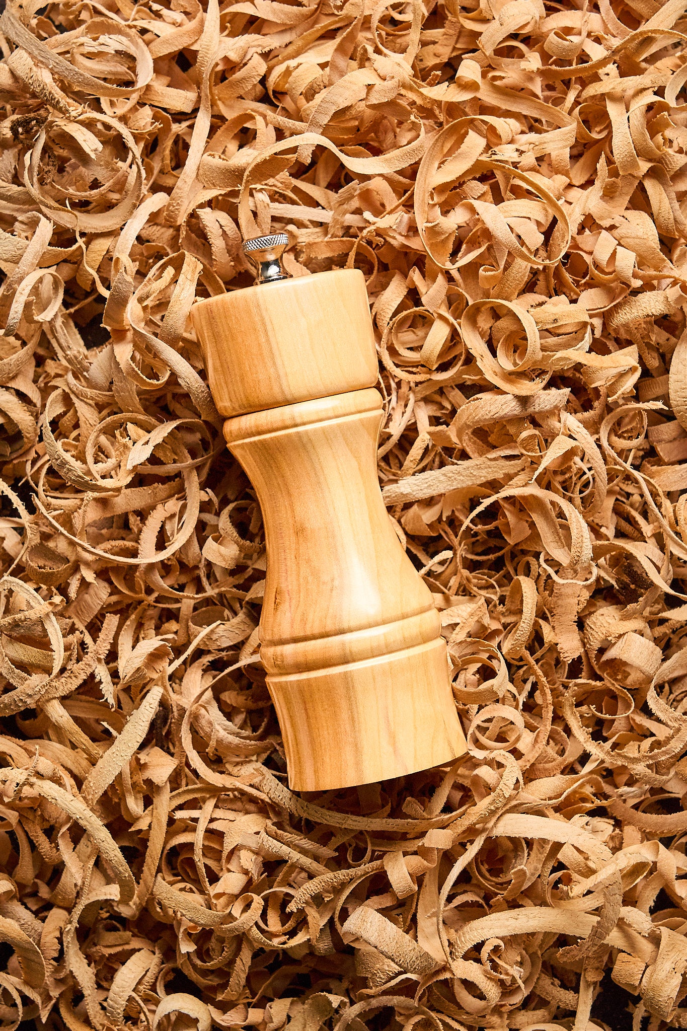 Modern pepper mill laying in a bed of wood shavings