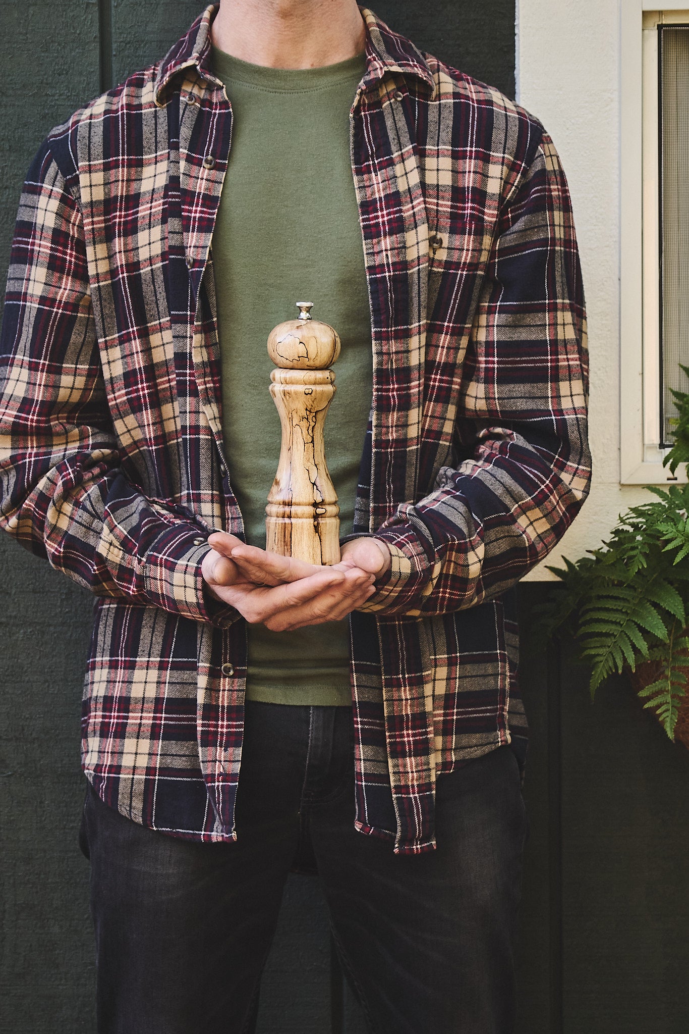 The maker holding the tall pepper mill handcrafted from salvaged apple wood