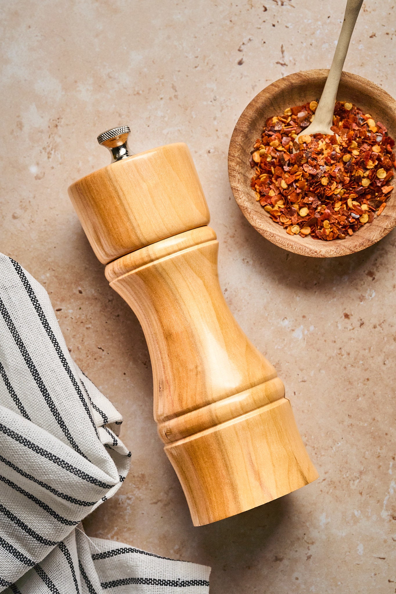The modern pepper mill next to a striped linen and a small bowl of red pepper flakes