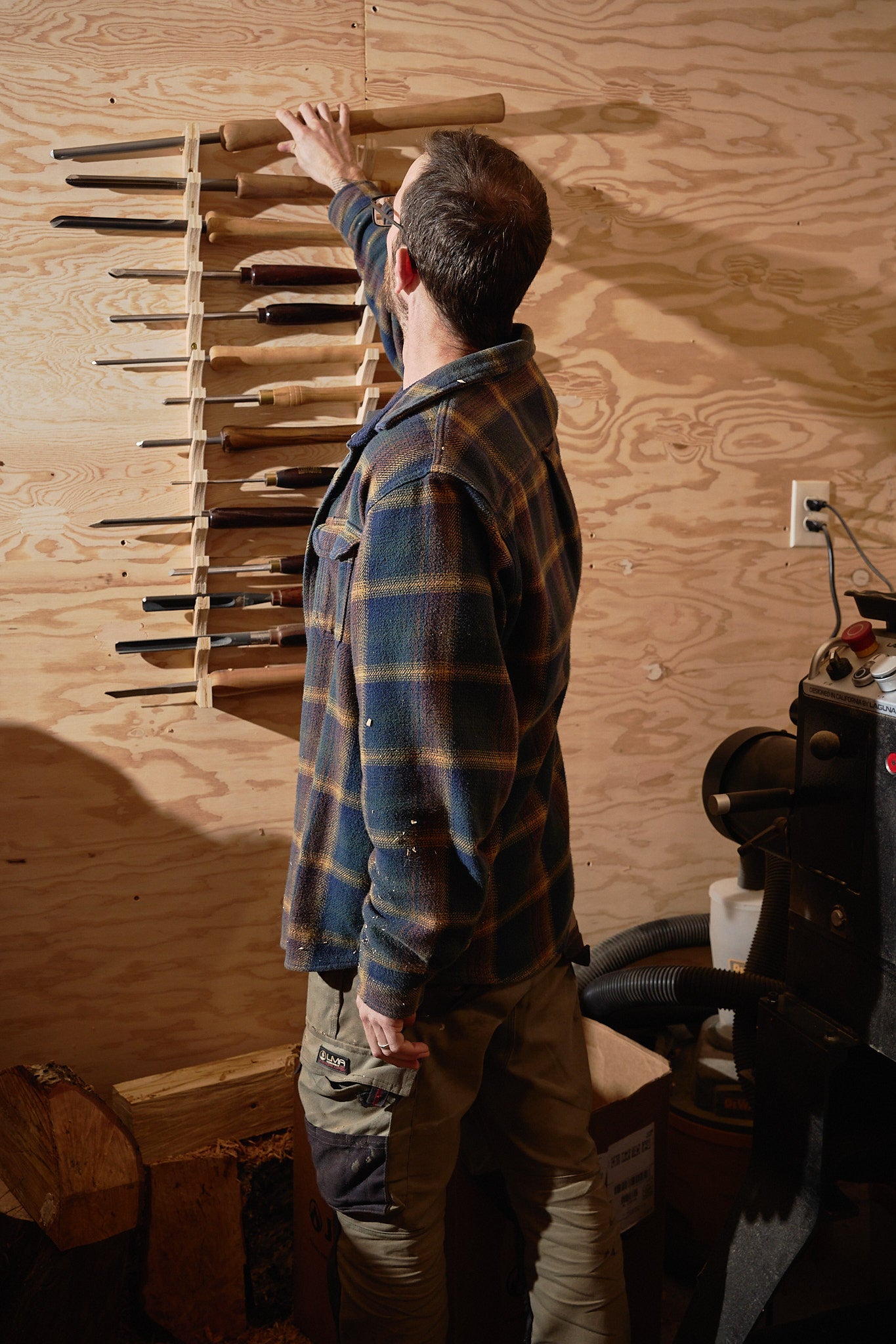 The wood turner reaching for his tools before he starts to turn the piece on his lathe.
