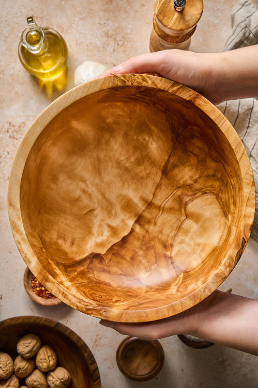 Big wood salad bowl held by hands, showcasing its handcrafted design and natural wood grain.