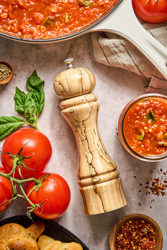 Top-down view of the tall pepper mill in-situe with marinara sauce, tomatoes, and fresh herbs